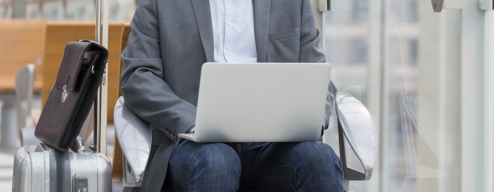 Cropped photo of a man with his luggage working on a laptop in an airport.